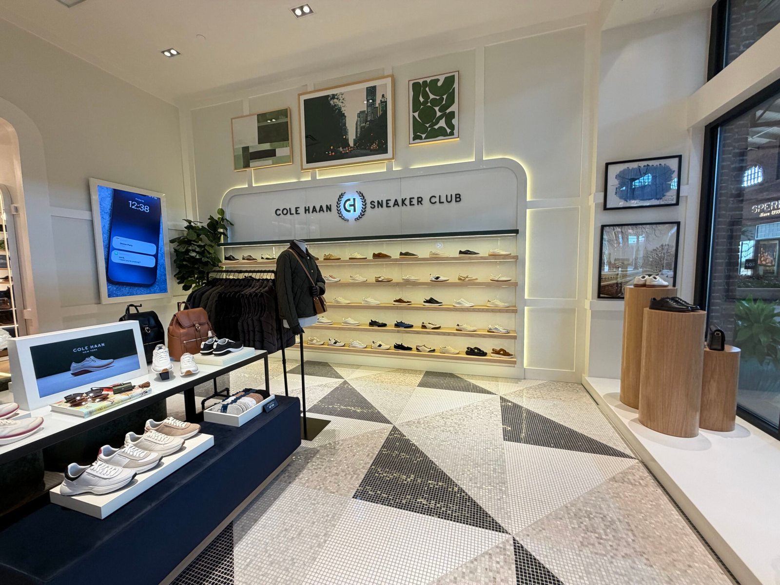 A lit wall of white and dark sneakers under a COLE HAAN SNEAKER CLUB sign, with more sneakers on a display table and patterned tile floor