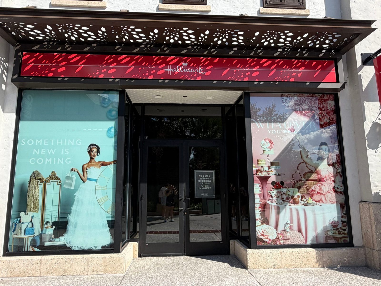 The Hallmark Holiday Pop-Up storefront at Disney Springs with a red Hallmark sign over the entrance, a Something New Is Coming window promo on the left and a Happily Whatever You're After promo on the right