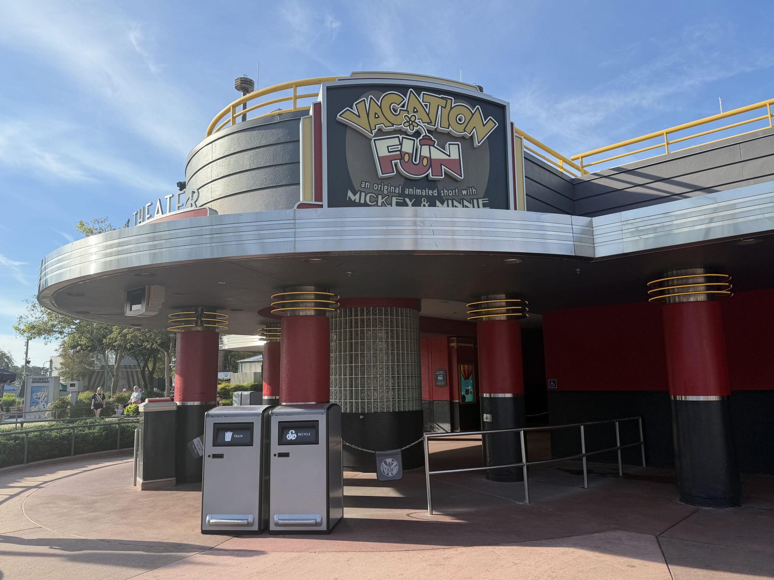 The Vacation Fun marquee reading an original animated short with Mickey and Minnie above the Mickey Shorts Theater entrance, with red and black columns, a glass block pillar and trash and recycling bins
