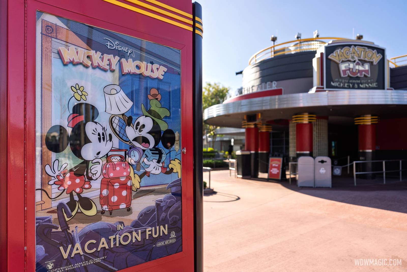 A Mickey Mouse in Vacation Fun poster showing Minnie with polka-dot luggage and Mickey holding a tennis racket, with the Vacation Fun marquee on the Mickey Shorts Theater behind it