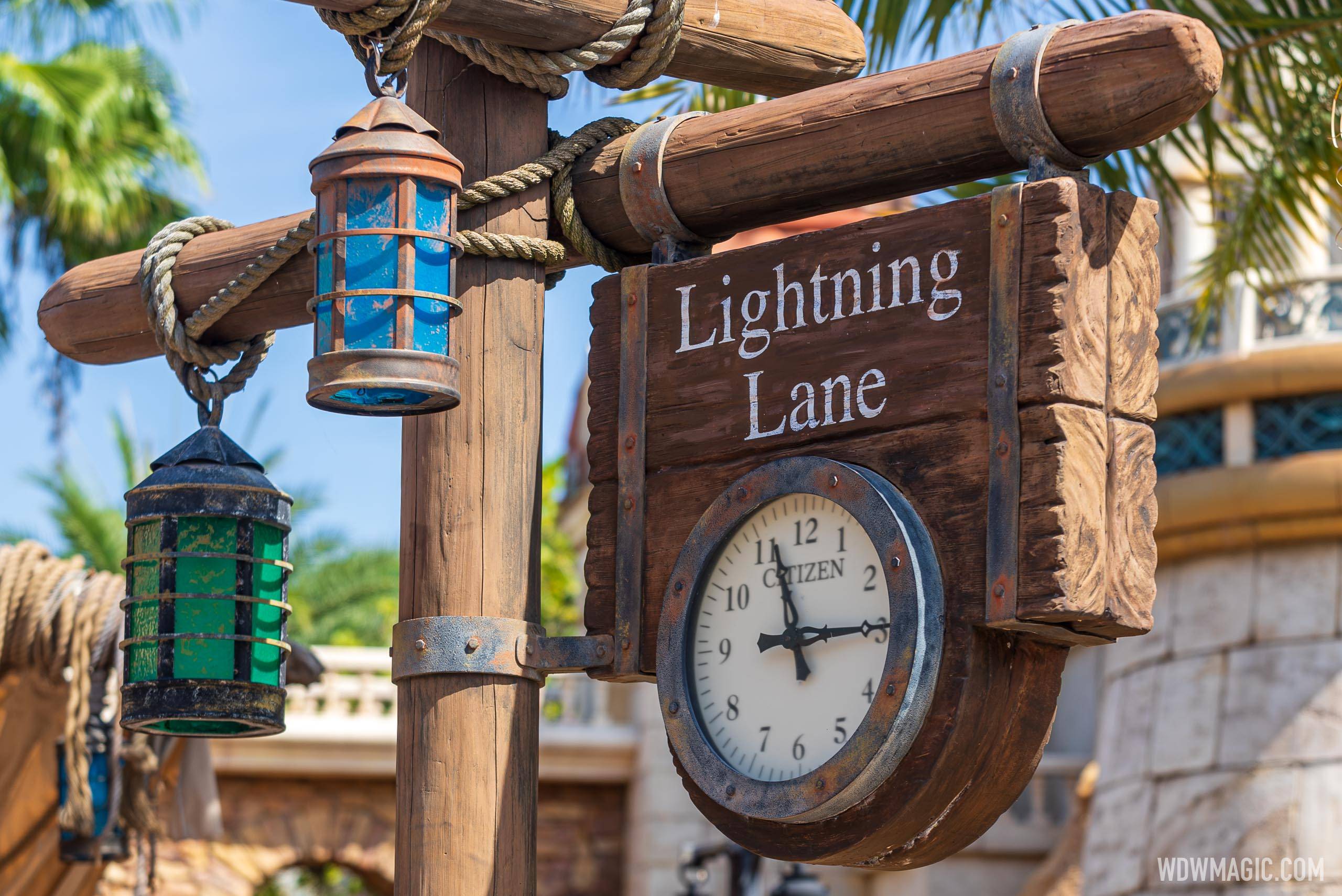 A carved wooden Lightning Lane sign with a round analog clock mounted below it, hanging from a wooden post with rope-wrapped beams and blue and green lanterns