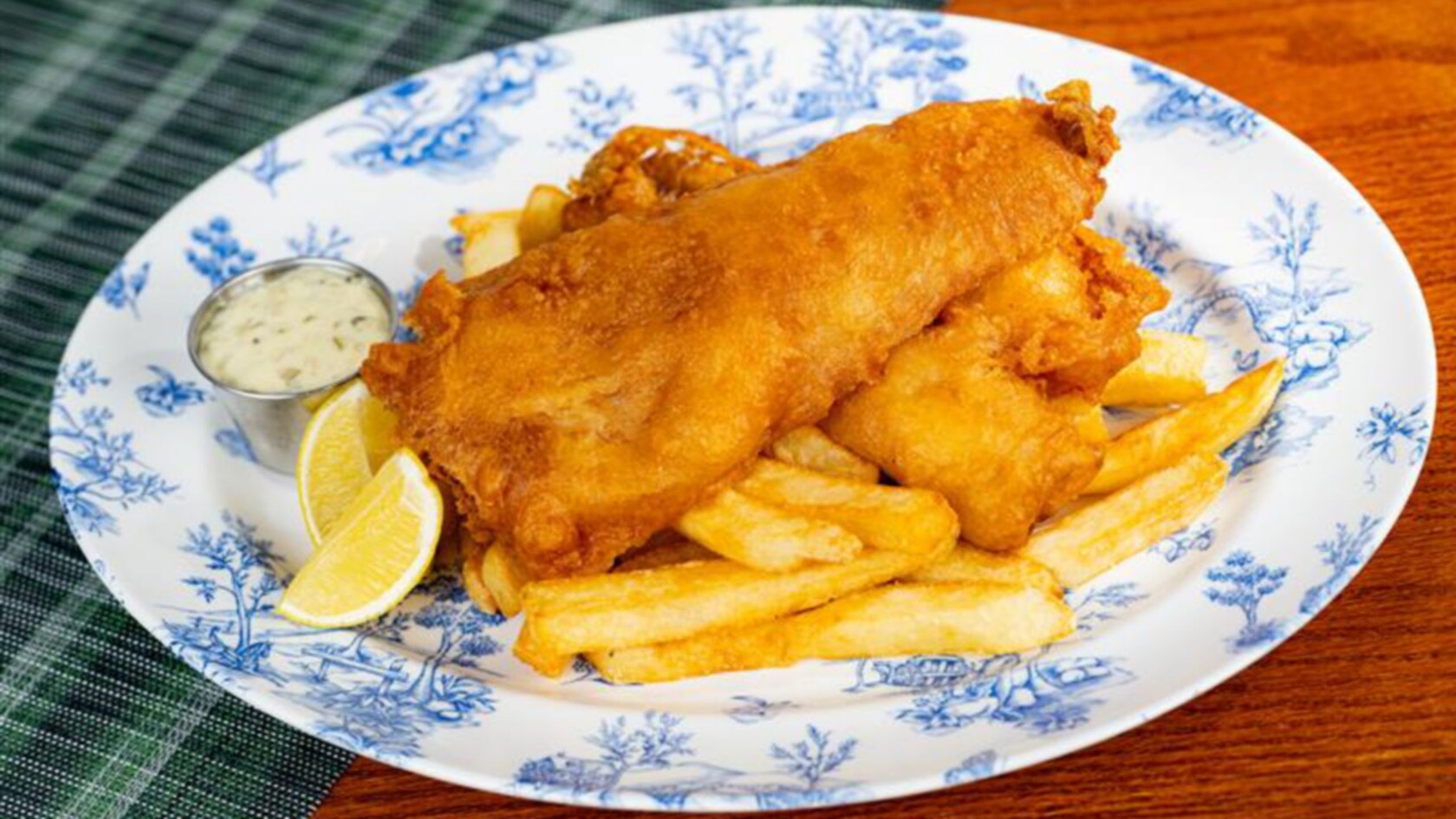 Beer-battered fish and chips with lemon wedges and a cup of tartar sauce on a blue and white patterned plate