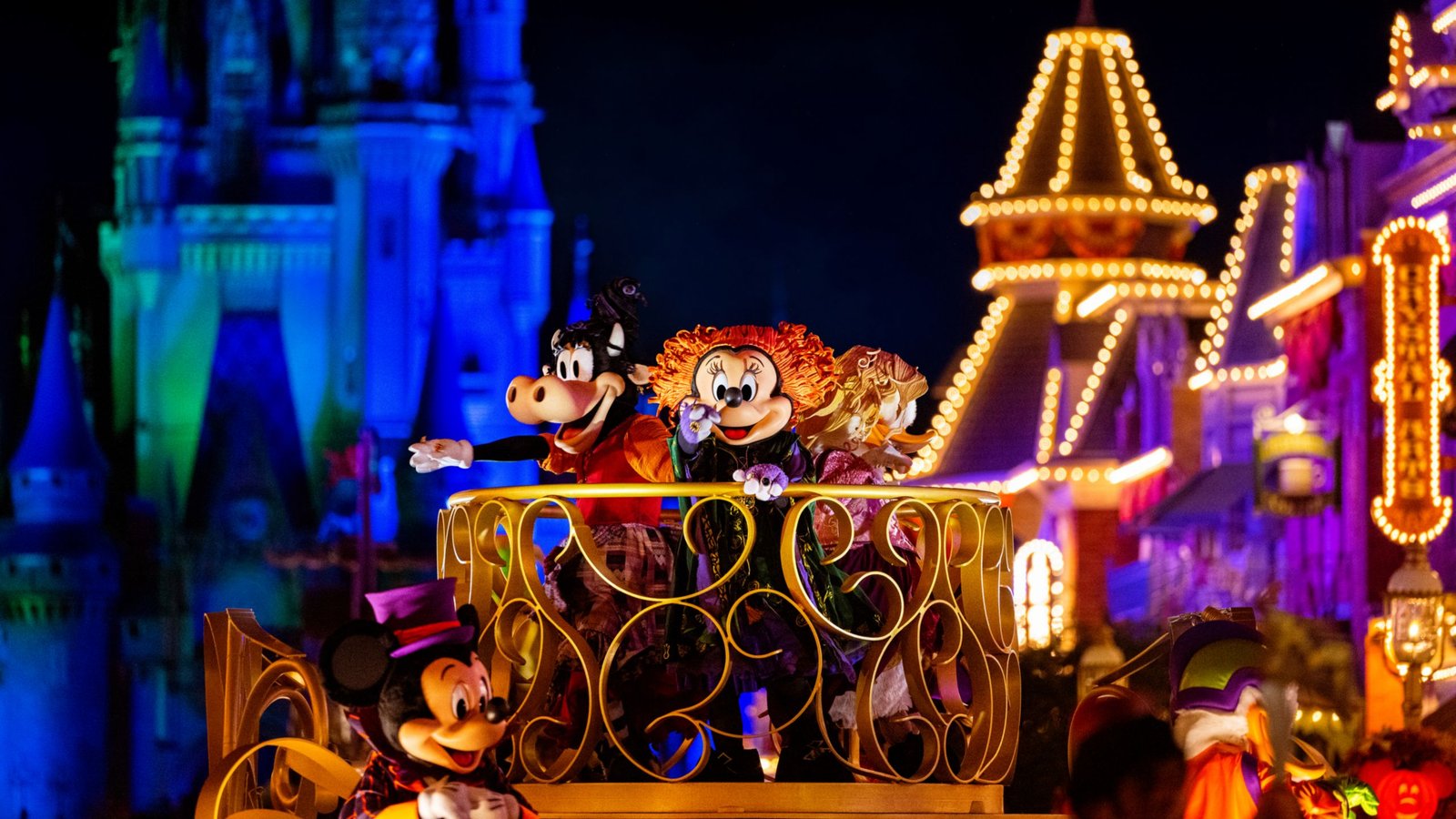 Mickey Mouse, Minnie Mouse and Clarabelle Cow in Halloween costumes on a gold parade float on Main Street, U.S.A., with a blue-lit Cinderella Castle behind them