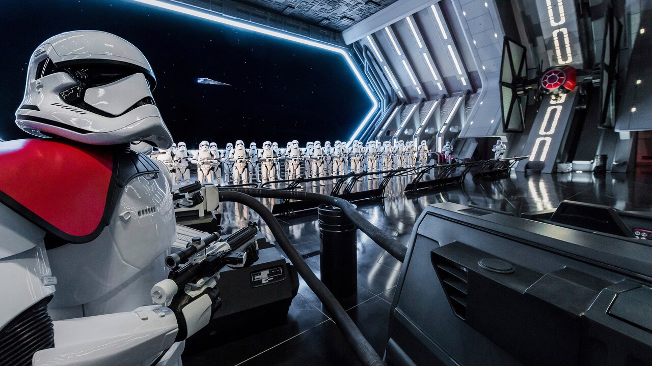 Rows of First Order stormtroopers stand at attention in a gleaming Star Destroyer hangar, with a TIE fighter on the right and a stormtrooper with a red shoulder pauldron in the foreground