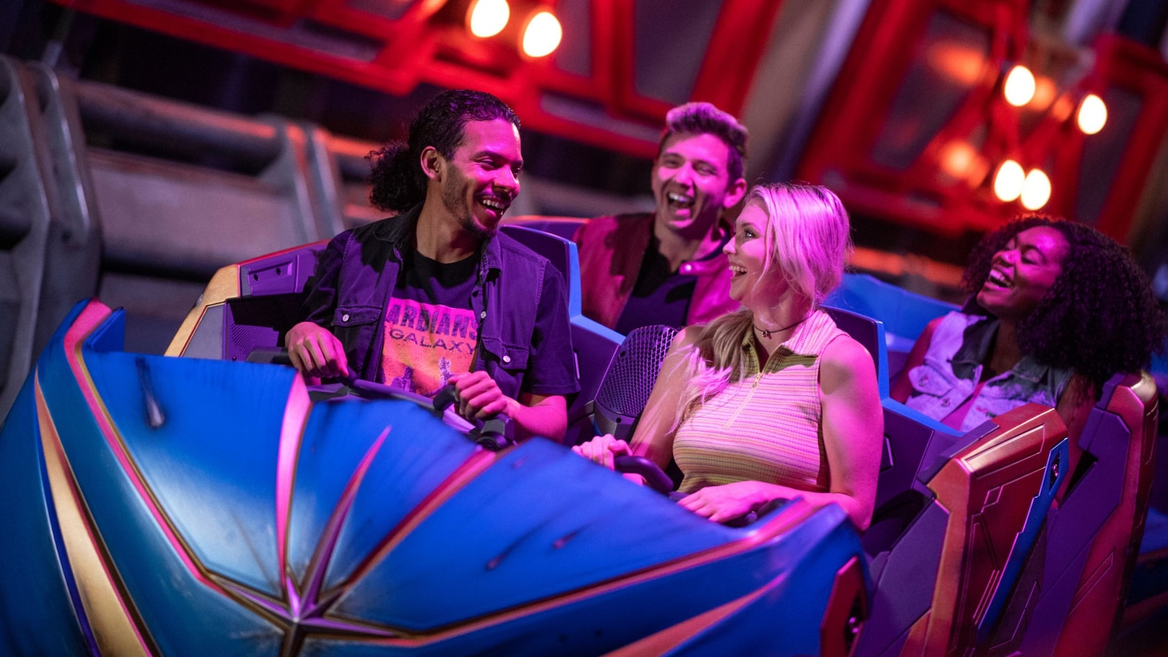 Four laughing guests ride in a blue and purple Guardians of the Galaxy: Cosmic Rewind vehicle under red lights