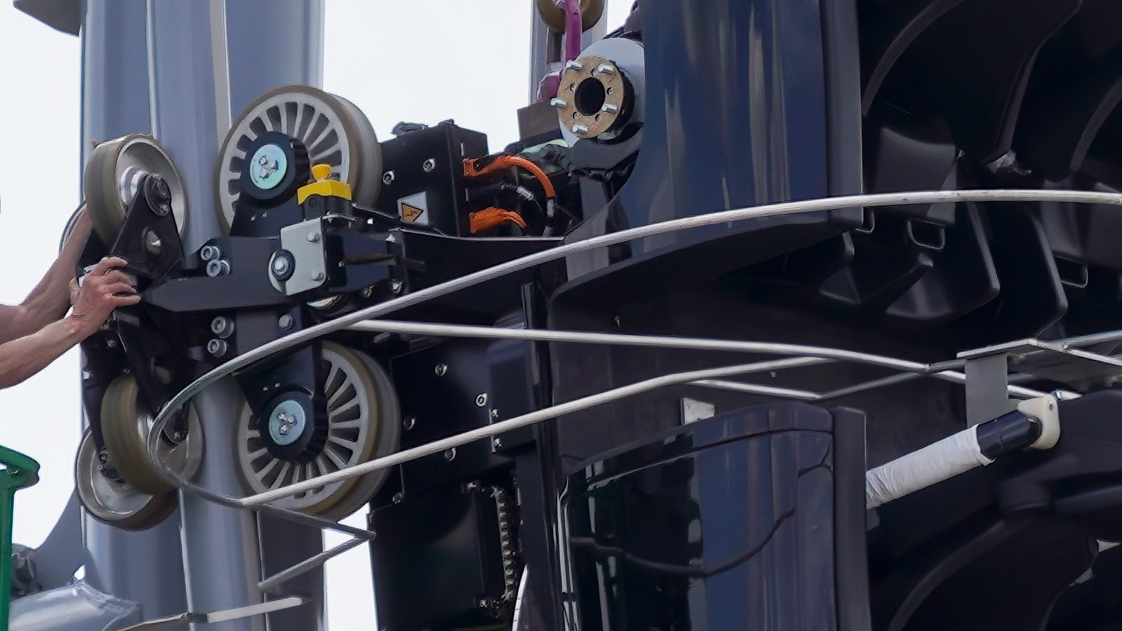Close-up of a worker's hands on a wheel assembly of the black test vehicle, with wheels, brackets and wiring visible beside a gray track rail