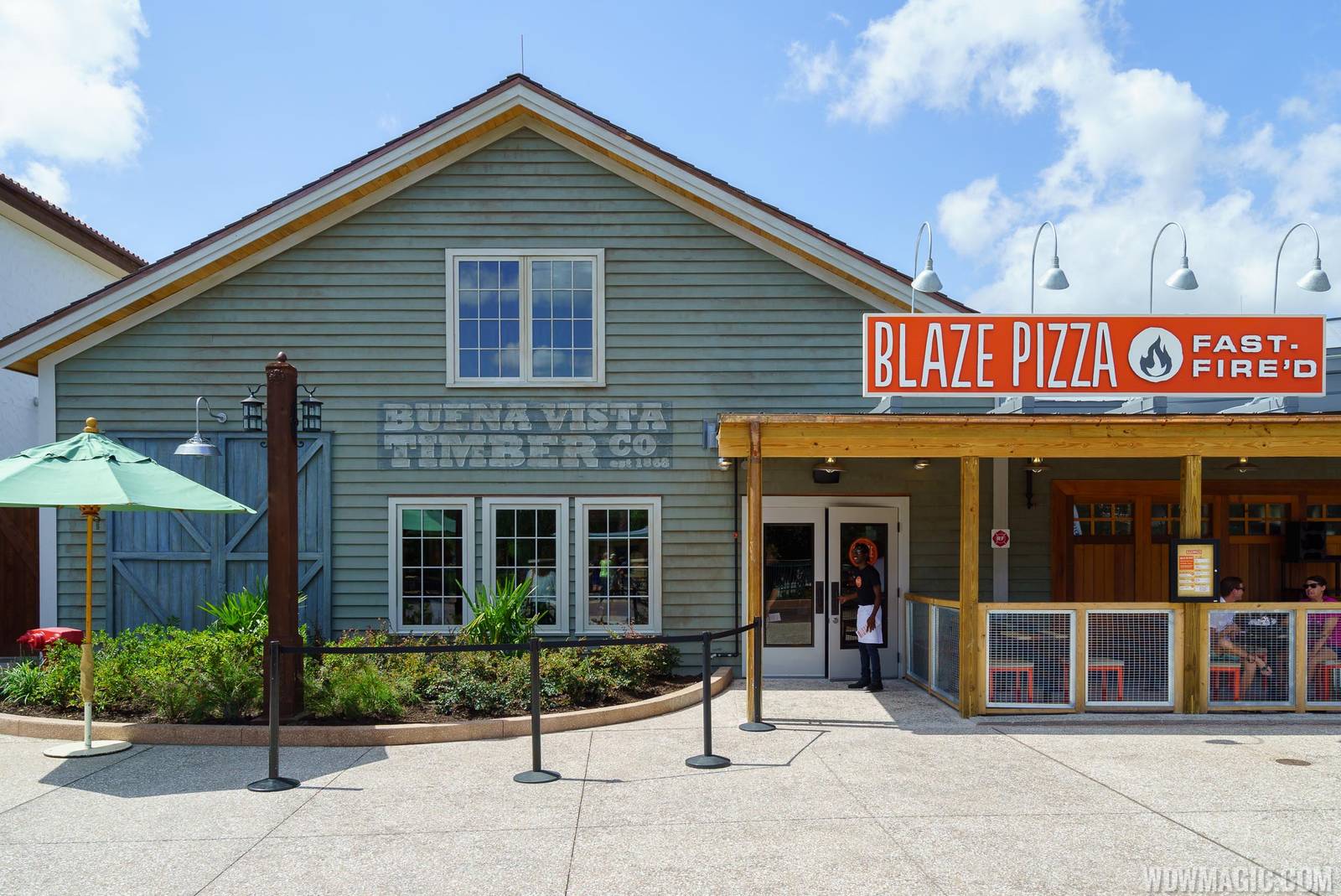 The front of Blaze Pizza at Disney Springs: an orange BLAZE PIZZA FAST-FIRE'D sign over a covered porch with orange chairs, beside a sage-green clapboard building painted with a faded Buena Vista Timber Co. sign