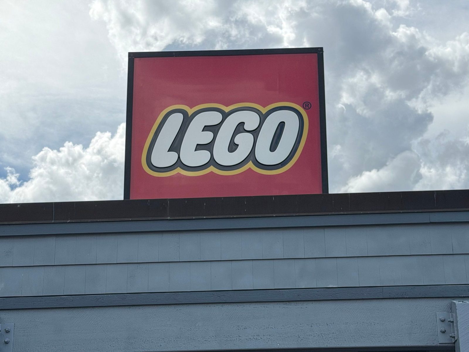 The red LEGO logo sign on the roofline of The LEGO Store at Disney Springs, set above grey-blue wood siding against a cloudy sky