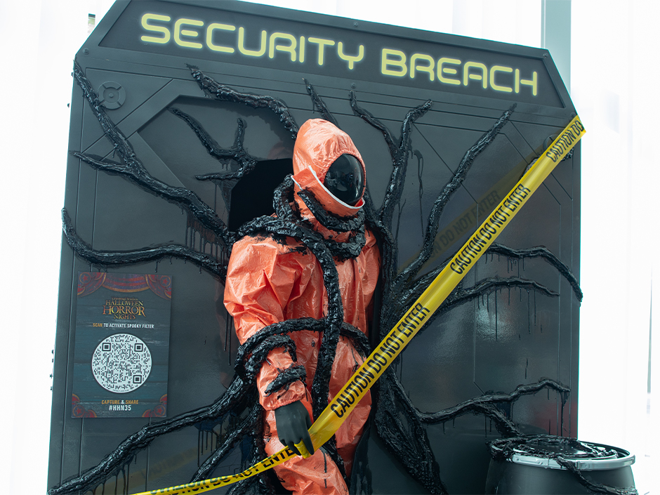 A figure in an orange hazmat suit wrapped in black tendrils stands in front of a dark panel reading SECURITY BREACH, with yellow caution tape across it
