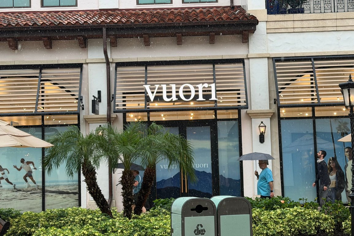 White Vuori lettering above the louvered windows of a Spanish-style storefront with palm trees and a tile roof, on a rainy day