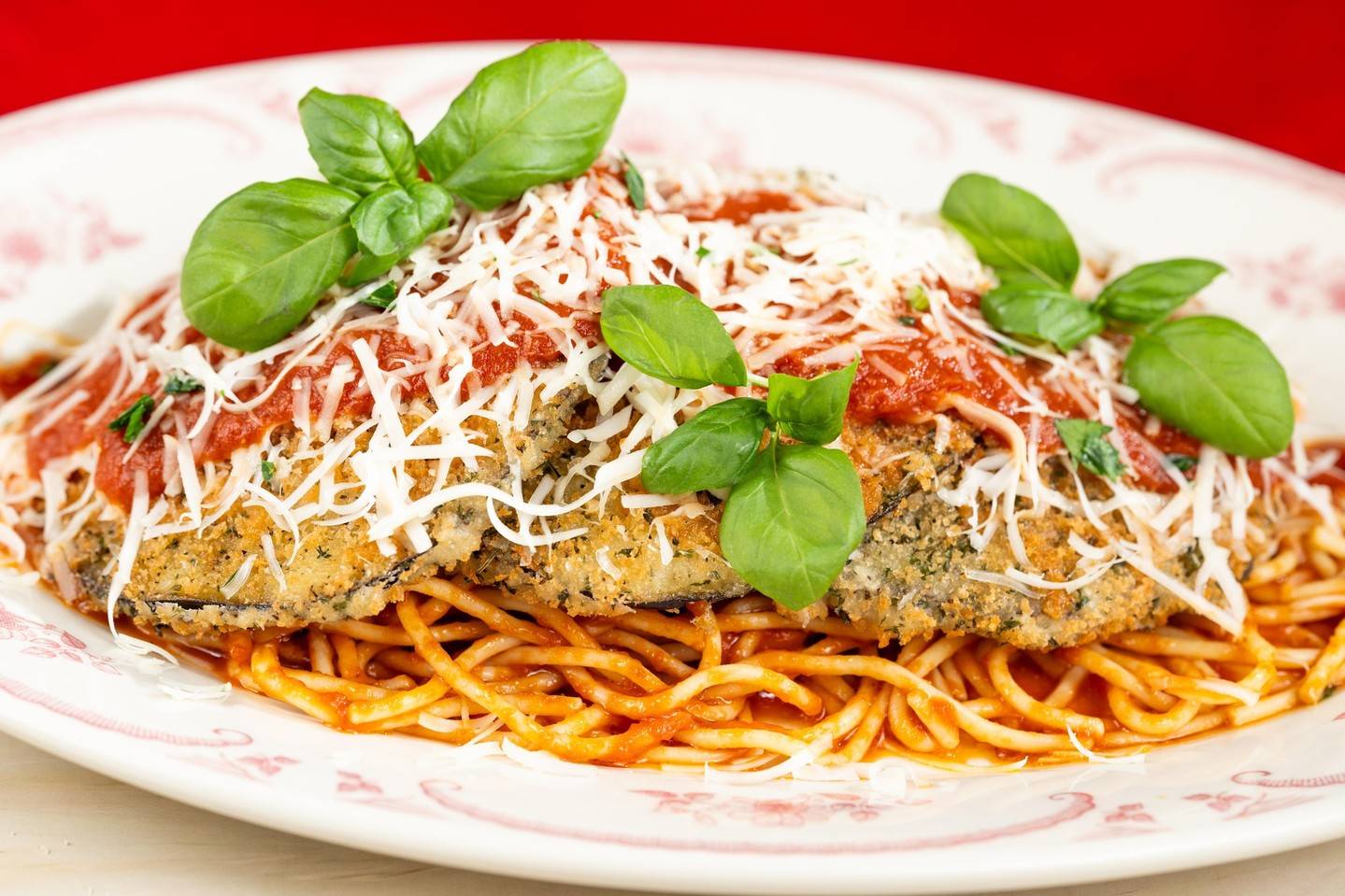 Breaded eggplant cutlet topped with marinara, shredded cheese and basil leaves over a bed of spaghetti in tomato sauce