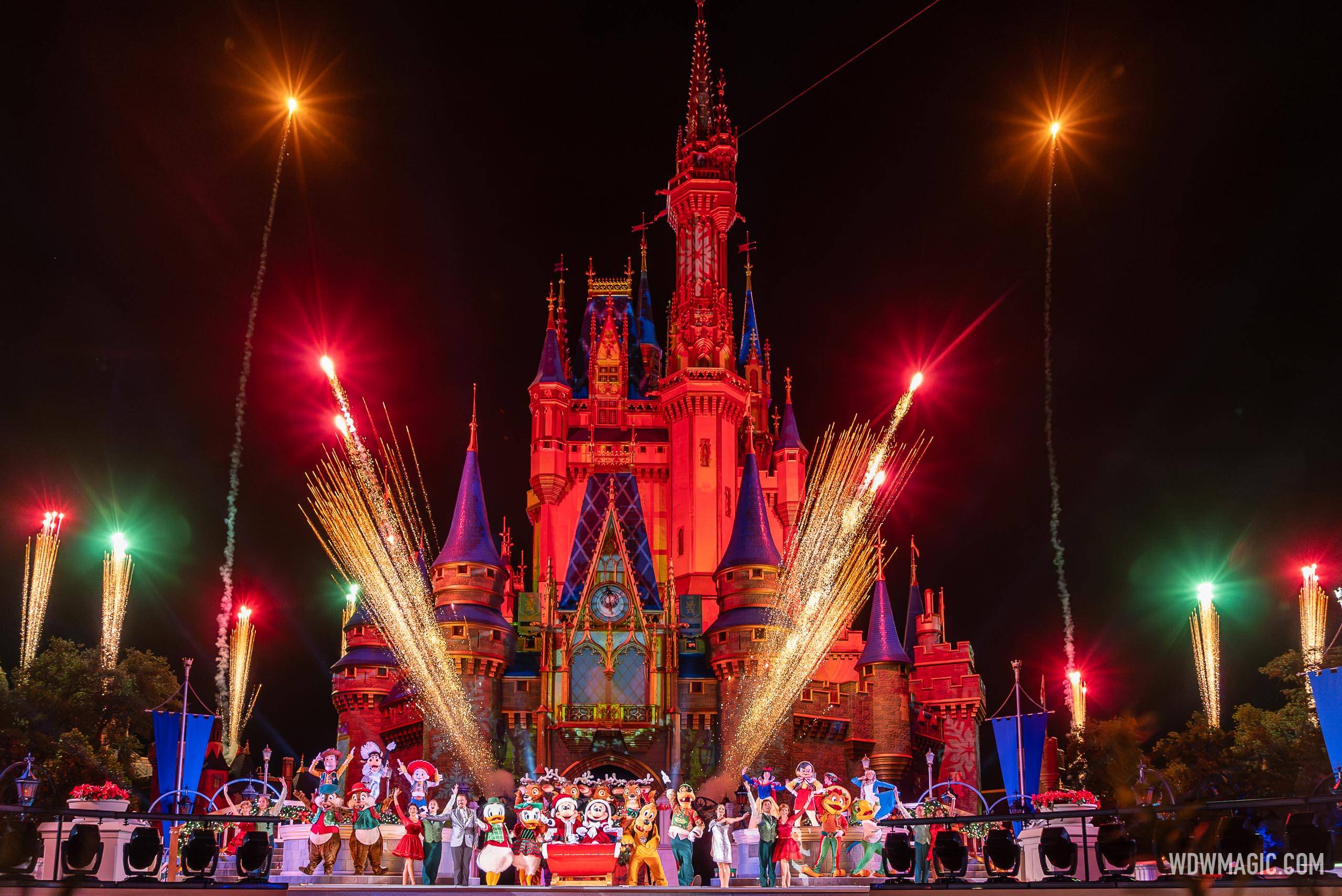 Cinderella Castle lit red at night with fireworks and golden sparkler effects, as Mickey and Minnie in a sleigh, Donald, Daisy, Goofy, Pluto, Chip and Dale, Woody, Jessie and other characters wave from the stage in front of it