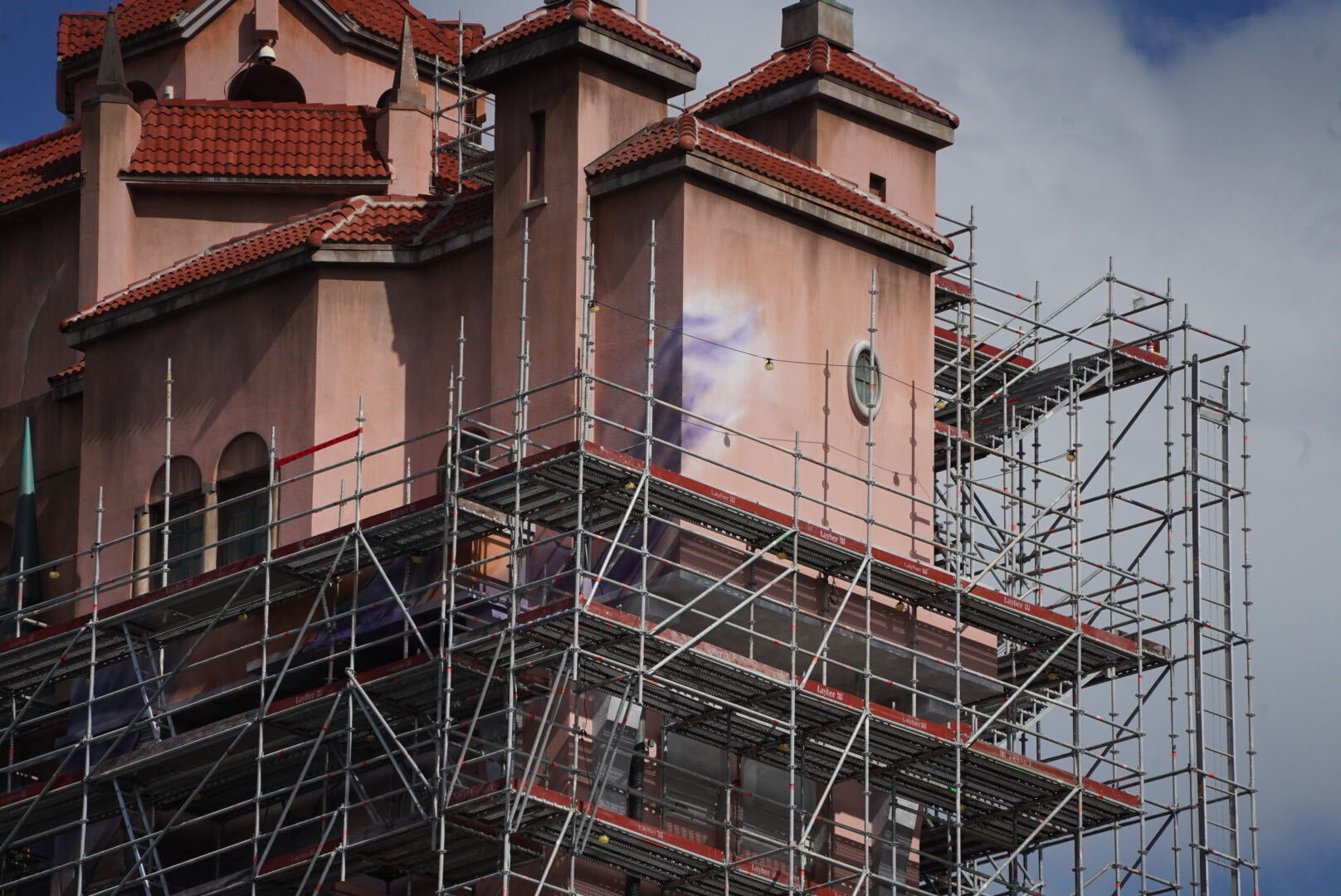Upper floors of the pink Hollywood Tower Hotel behind scaffolding, with a streak of purple and white paint spreading across the wall beside a small round window