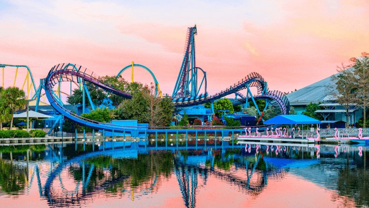 Mako's blue and purple track and lift hill under a pink and orange sunset sky, reflected in the still lagoon in front of SeaWorld Orlando