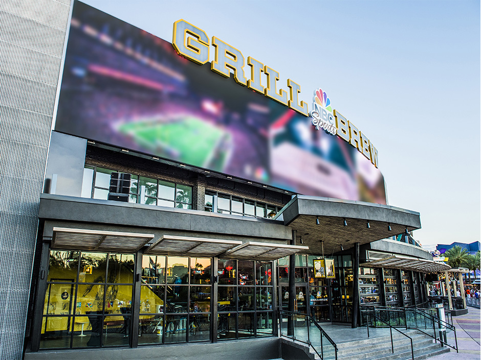 The exterior of NBC Sports Grill and Brew at Universal CityWalk, with large Grill and Brew letters and an NBC peacock above a giant video screen showing a blurred sports broadcast
