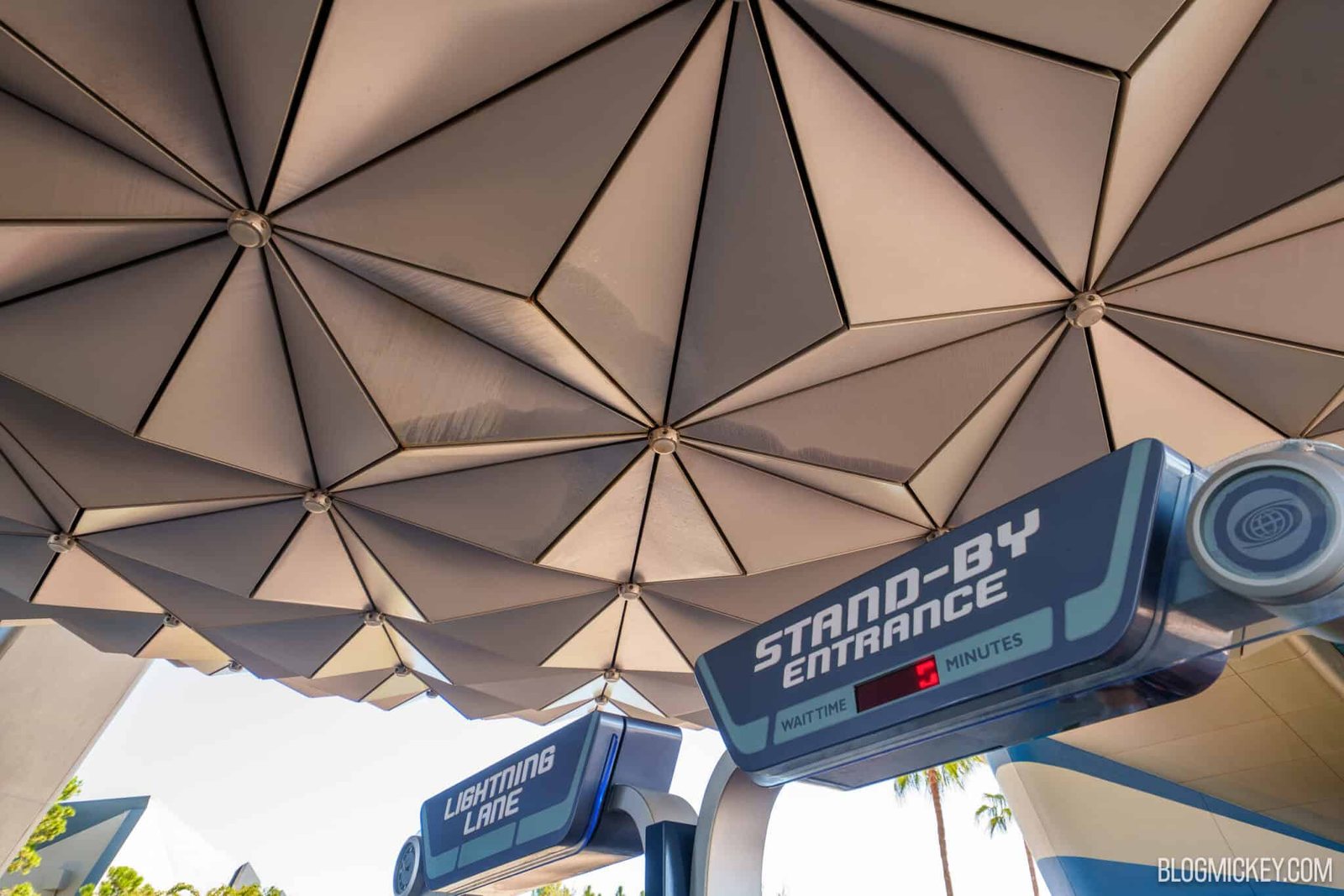Looking up at the faceted underside of the Spaceship Earth sphere above the Stand-By Entrance and Lightning Lane signs