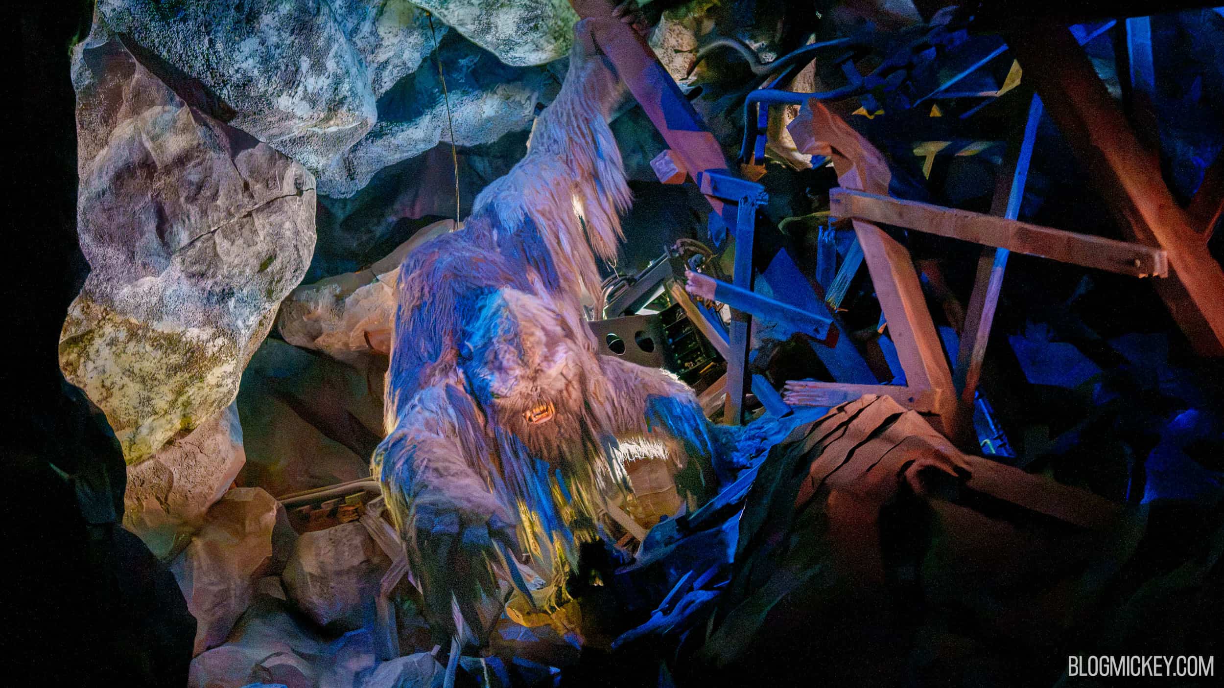 The Expedition Everest Yeti figure lit up among rocks and broken wooden beams, mouth open showing its fangs, with machinery visible in the shadows behind it