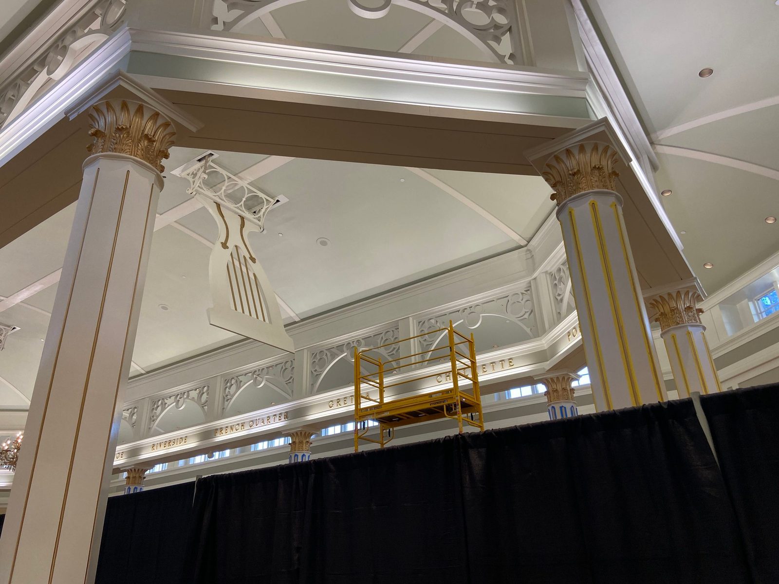 Looking up past white and gold columns over a black curtain line in the lobby, with a yellow work platform visible behind the curtains and ornate white ceiling trim above