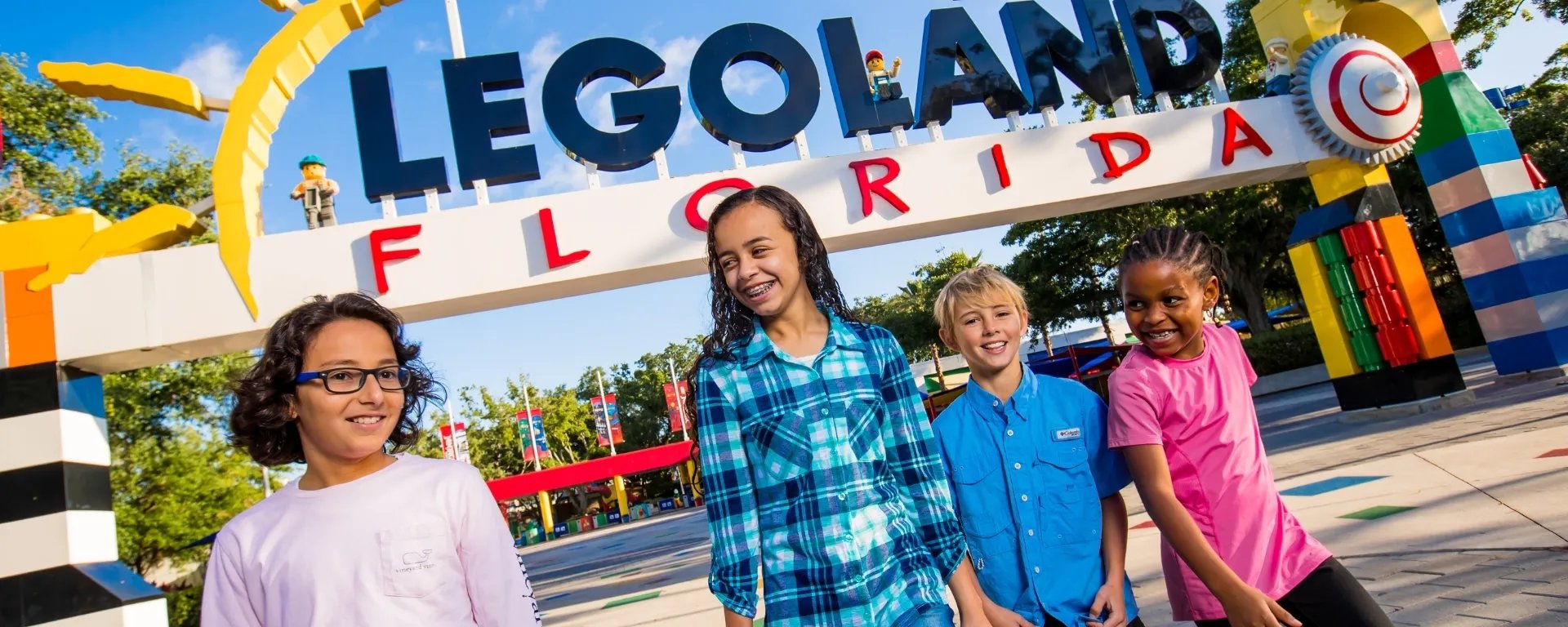 Four smiling kids walk under the colorful LEGOLAND Florida entrance arch, built to look like giant LEGO bricks