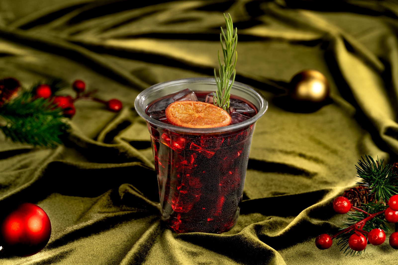 A clear cup of iced red mulled wine garnished with a dried orange slice and a rosemary sprig