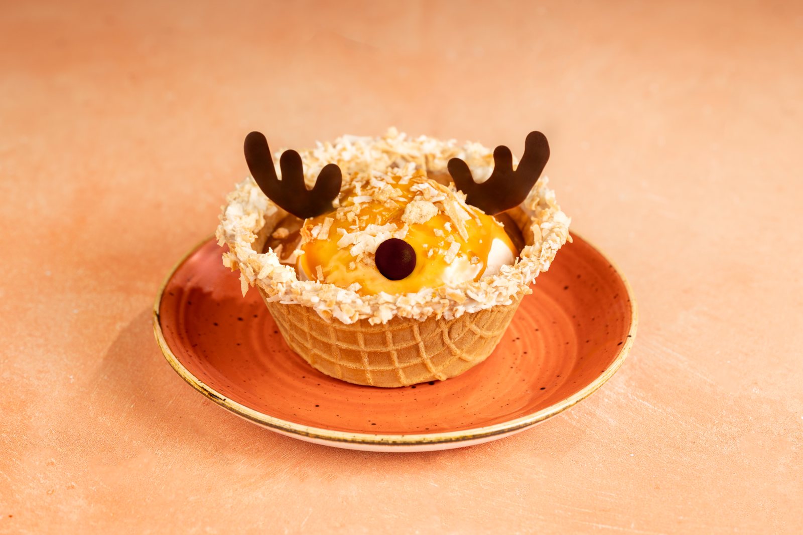 A sundae in a waffle bowl rimmed with toasted coconut, with caramel-drizzled ice cream, two chocolate antlers and a chocolate candy nose