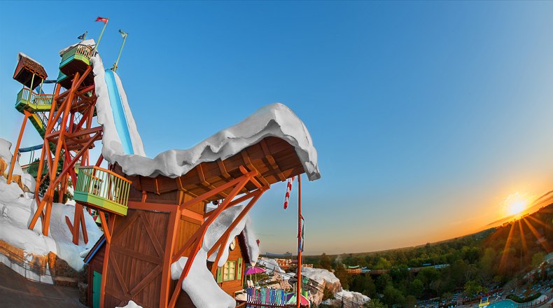Summit Plummet's tall orange ski-jump tower and snow-capped lodge roof at Disney's Blizzard Beach, photographed with a fisheye lens as the sun sets over the trees
