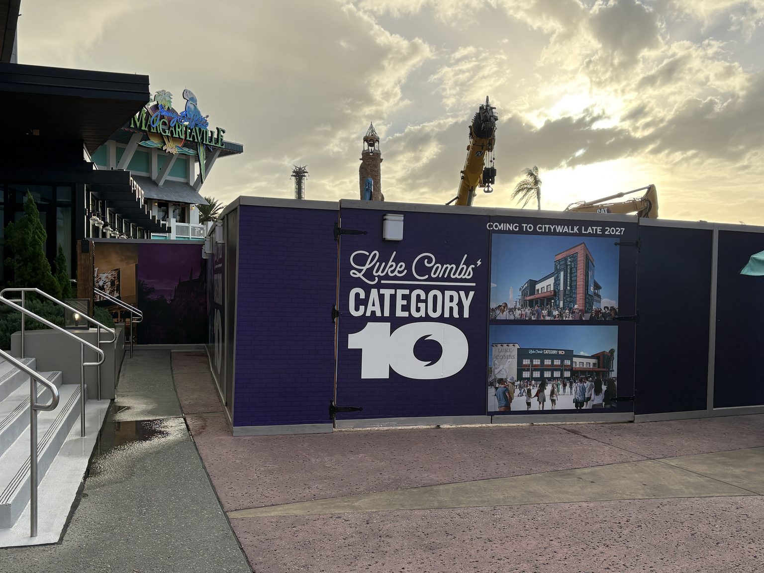 Purple construction walls printed with the Luke Combs' Category 10 logo and two building renderings under a Coming to CityWalk Late 2027 banner, with the Jimmy Buffett's Margaritaville sign on the left and a crane rising behind the wall