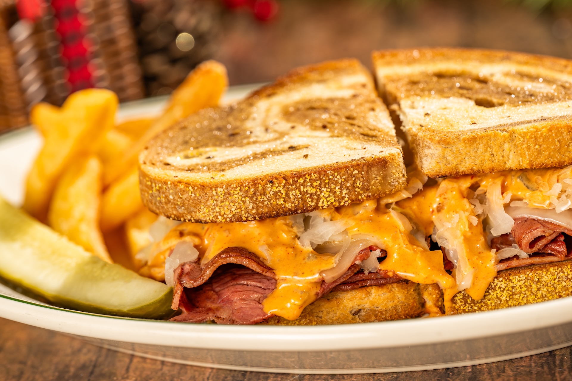A Reuben sandwich on toasted marbled rye, cut in half, with layers of corned beef, sauerkraut, melted Swiss cheese and orange dressing, served with fries and a pickle spear