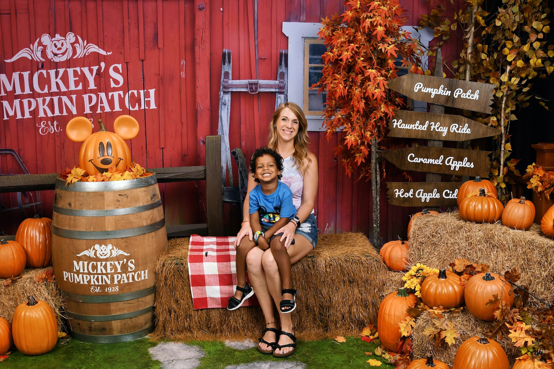 A parent and child posing at Mickey's Pumpkin Patch, a seasonal Disney PhotoPass backdrop with pumpkins and hay bales