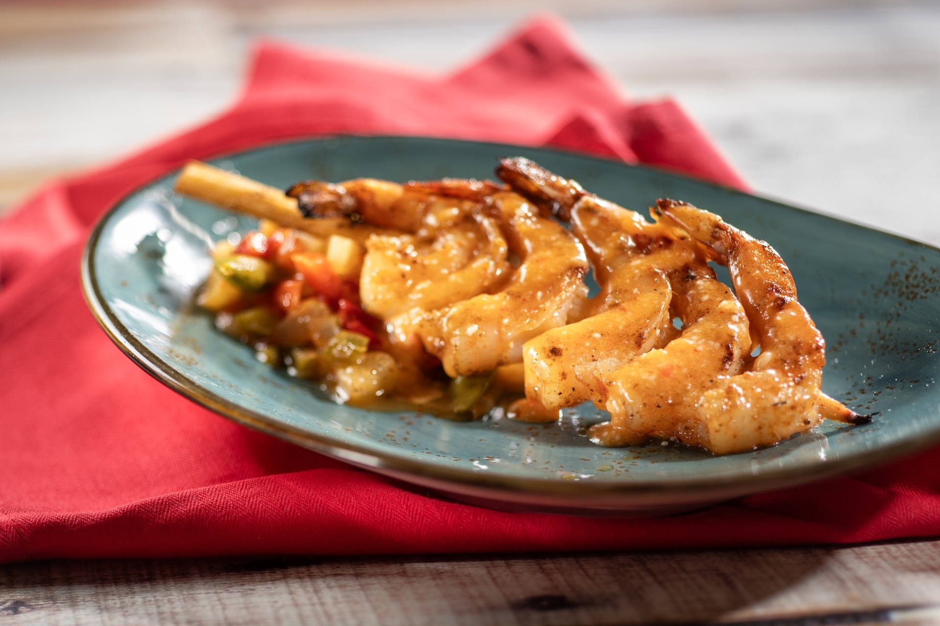 Grilled Bushberry-spiced Shrimp Skewer with sweet-and-sour vegetables and coconut-chili sauce on a black plate.