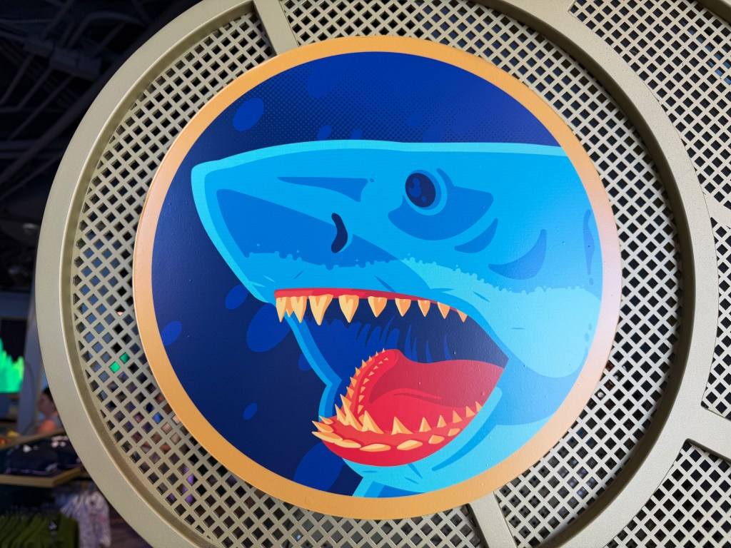 The Jaws photo op inside the Universal Legacy Store, with the shark lunging beside the Orca on Amity Island in a wraparound mural by Tom Whalen.